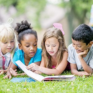 4 enfants lisant sur l'herbe