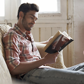 homme assis sur canapé lisant un livre