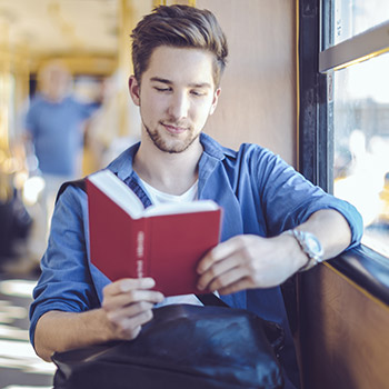 homme lisant un livre dans un train à côté de la fenêtre