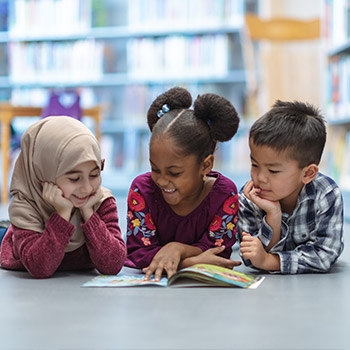 3 enfants allongés sur le sol d'une bibliothèque avec un livre