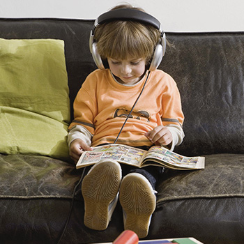 petit enfant assis sur un canapé lisant une BD avec un casque de musique sur la tête